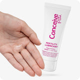 Conceive Plus Fertility Lubricant Pack (ES) featuring 75ml multi-use tube, shown with a close-up of a hand holding a small amount of clear lubricant next to white tube labeled in pink.