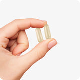 Conceive Plus Ovulation Bundle (ES) highlighting two beige Ovulation Support capsules delicately held between fingers, offering a clear view of their size, shape, and smooth vegetarian capsule texture for user familiarity.